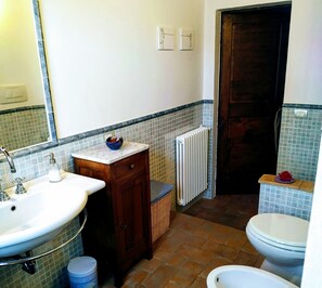 Bathroom features a sink, mirror, toilet, and radiator, with a wicker basket and trash bin nearby.