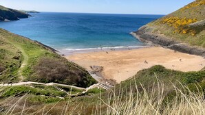 Eine K üstenlandschaft mit sandigem Strand, blauem Meer und sanften Hügeln.