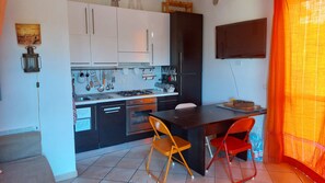 Une cuisine compacte avec des meubles blancs et noirs, une cuisinière à gaz et un coin repas comprenant une table et deux chaises.