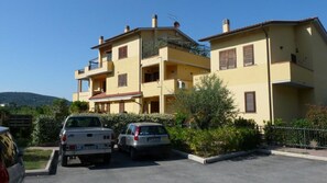 Un immeuble résidentiel de deux étages, avec une façade jaune, de nombreux balcons et des voitures garées dans l’allée.