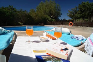 A poolside table with two glasses of orange juice, a bowl of snacks, and a book titled "The Art of Happiness". - Country cottage EL Olivar - El Orujo (Santa Lucía de Tirajana)