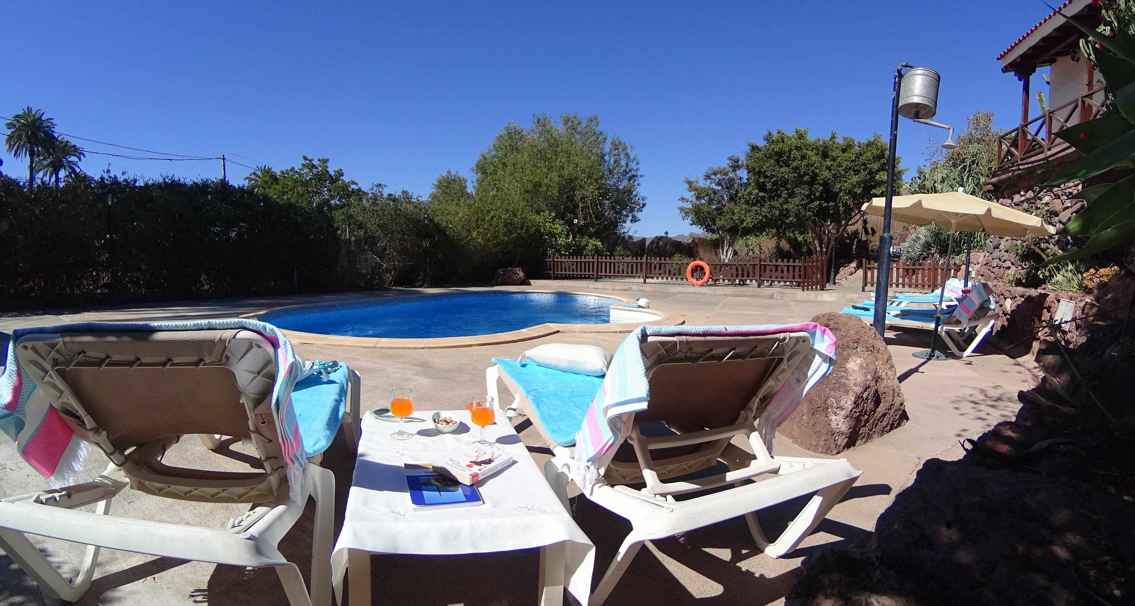 A poolside area with lounge chairs, a table with breakfast items, and a clear blue sky.