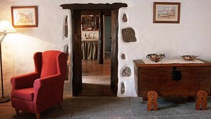 Una habitación con un sillón rojo, una mesa de madera con un cuenco y una pared de piedra con un marco de cuadro.