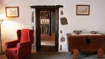 A room with a red armchair, a wooden table with a bowl, and a stone wall with a picture frame.