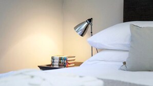 A neatly made bed with white linens, a bedside lamp, and a stack of books on a nightstand. - Stylish Apt in Heart of Georgian Bath (WST) (Bath)