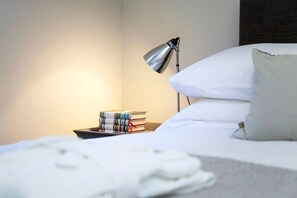 A neatly made bed with white linens, a bedside lamp, and a stack of books on a nightstand. - Stylish Apt in Heart of Georgian Bath (WST) (Bath)