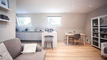 A modern living space with a sofa, dining table, chairs, a kitchen area, and built-in shelving.
