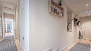 A hallway with a striped rug, a wooden shelf with books, and a door. - Stylish Apt in Heart of Georgian Bath (WST) (Bath)