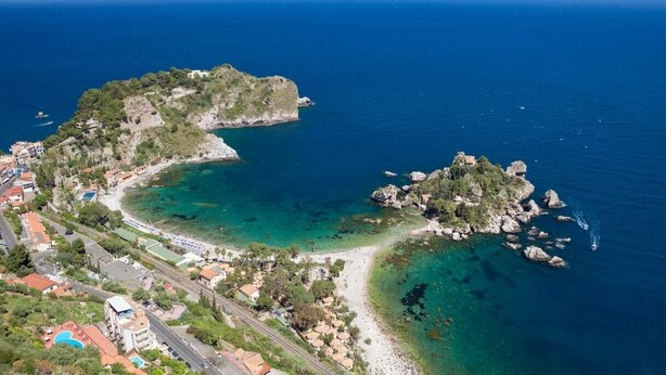 Une vue aérienne d’une zone côtière avec une petite île, des eaux d’un bleu limpide et une plage.