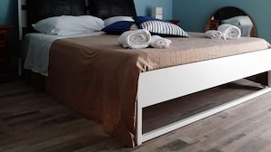 Une chambre à coucher avec un lit, deux tableaux encadrés au mur, un luminaire au plafond et un appareil de climatisation.