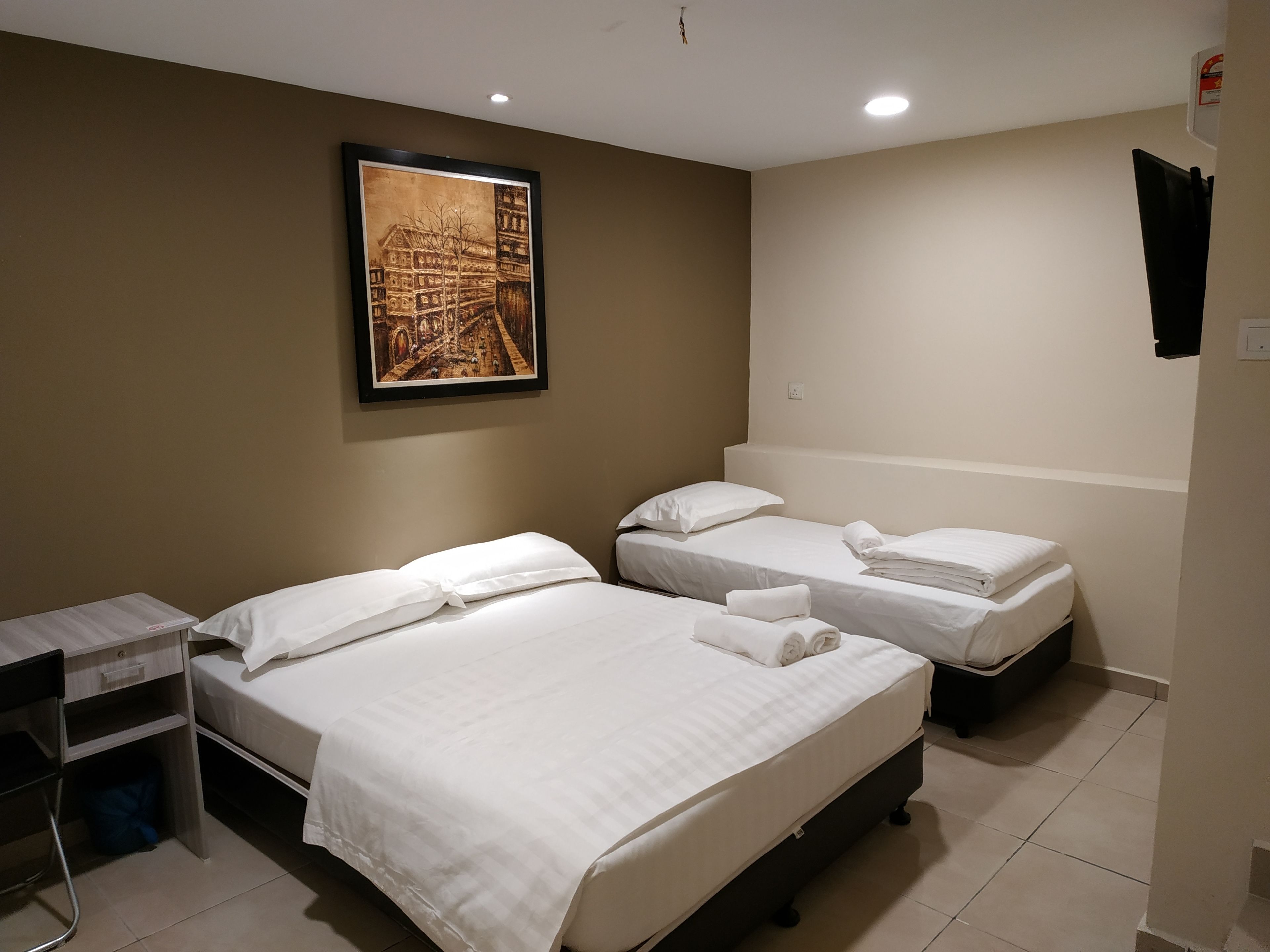 Quarto de hotel com duas camas, uma escrivaninha e um quadro pendurado na parede.