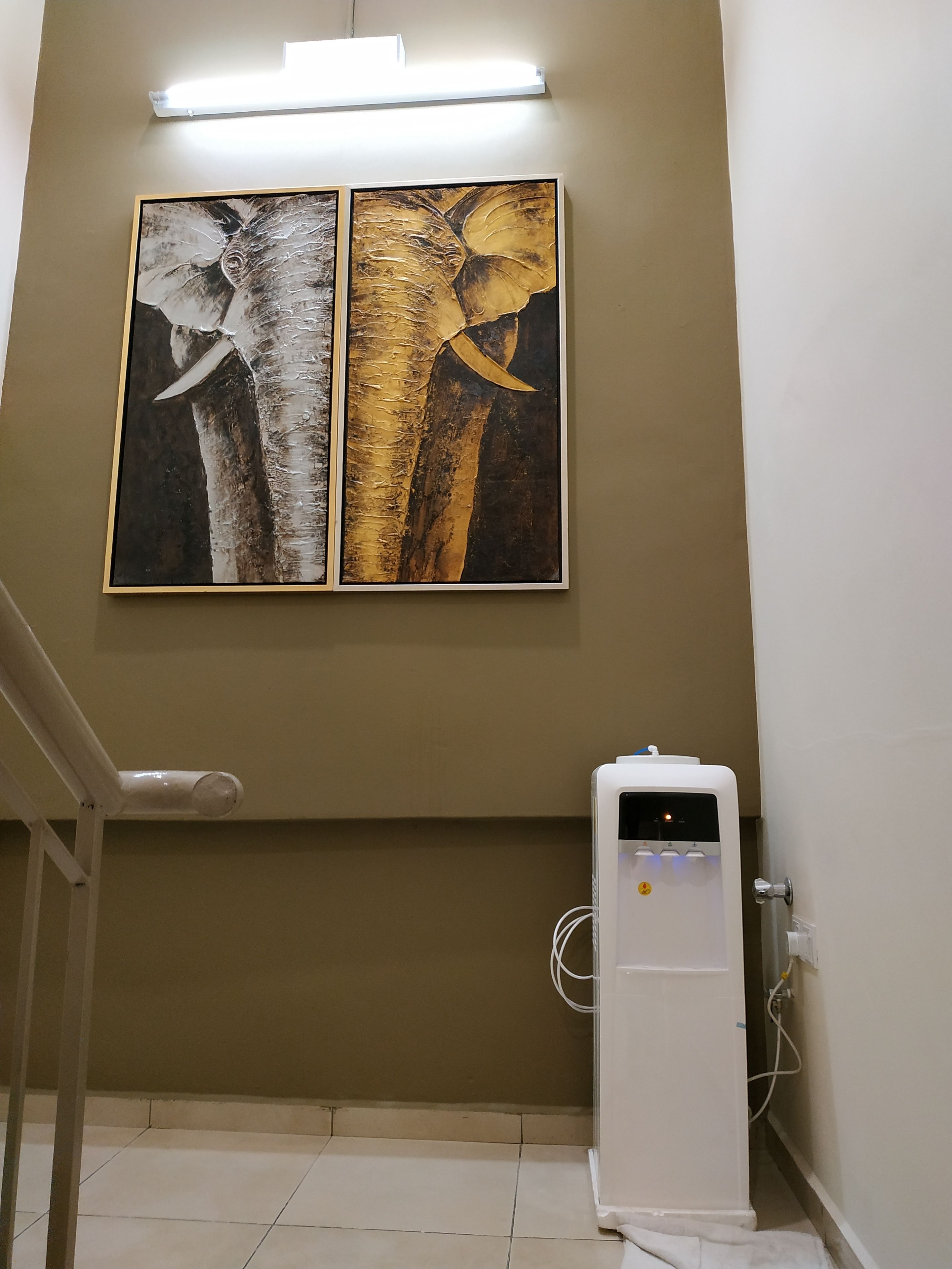 A room with a wall-mounted air conditioning unit and two framed paintings of elephants.