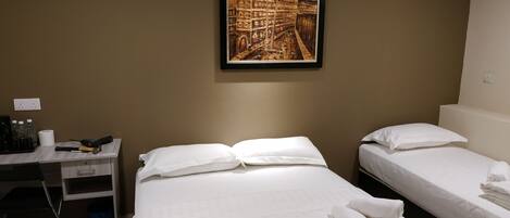 Une chambre d’hôtel avec deux lits simples, un bureau avec une chaise, un tableau encadré au mur et une petite poubelle.