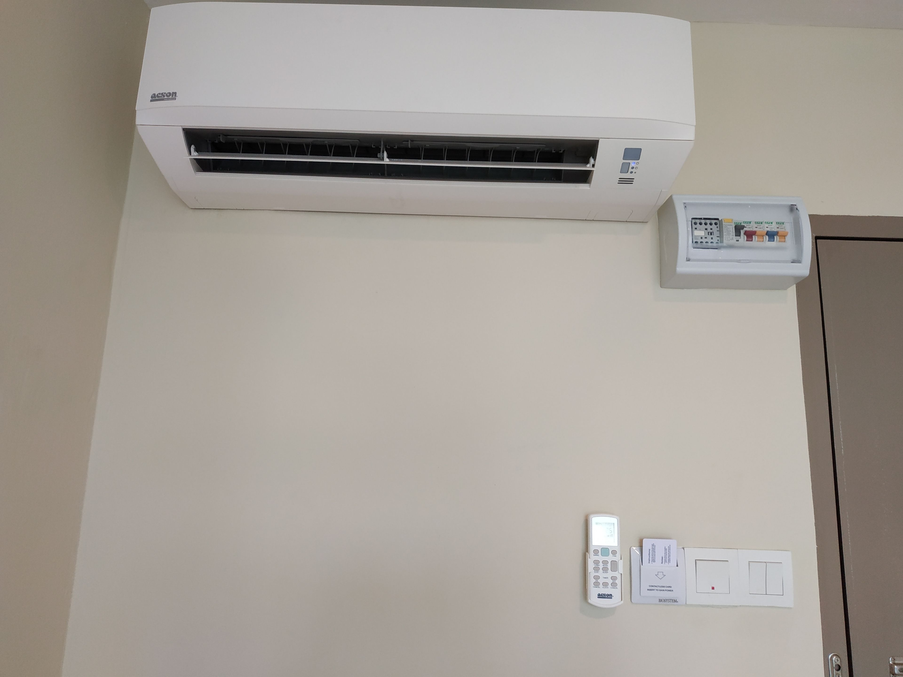 A white air conditioning unit mounted on a wall, a control panel with a remote, and a door with a handle.