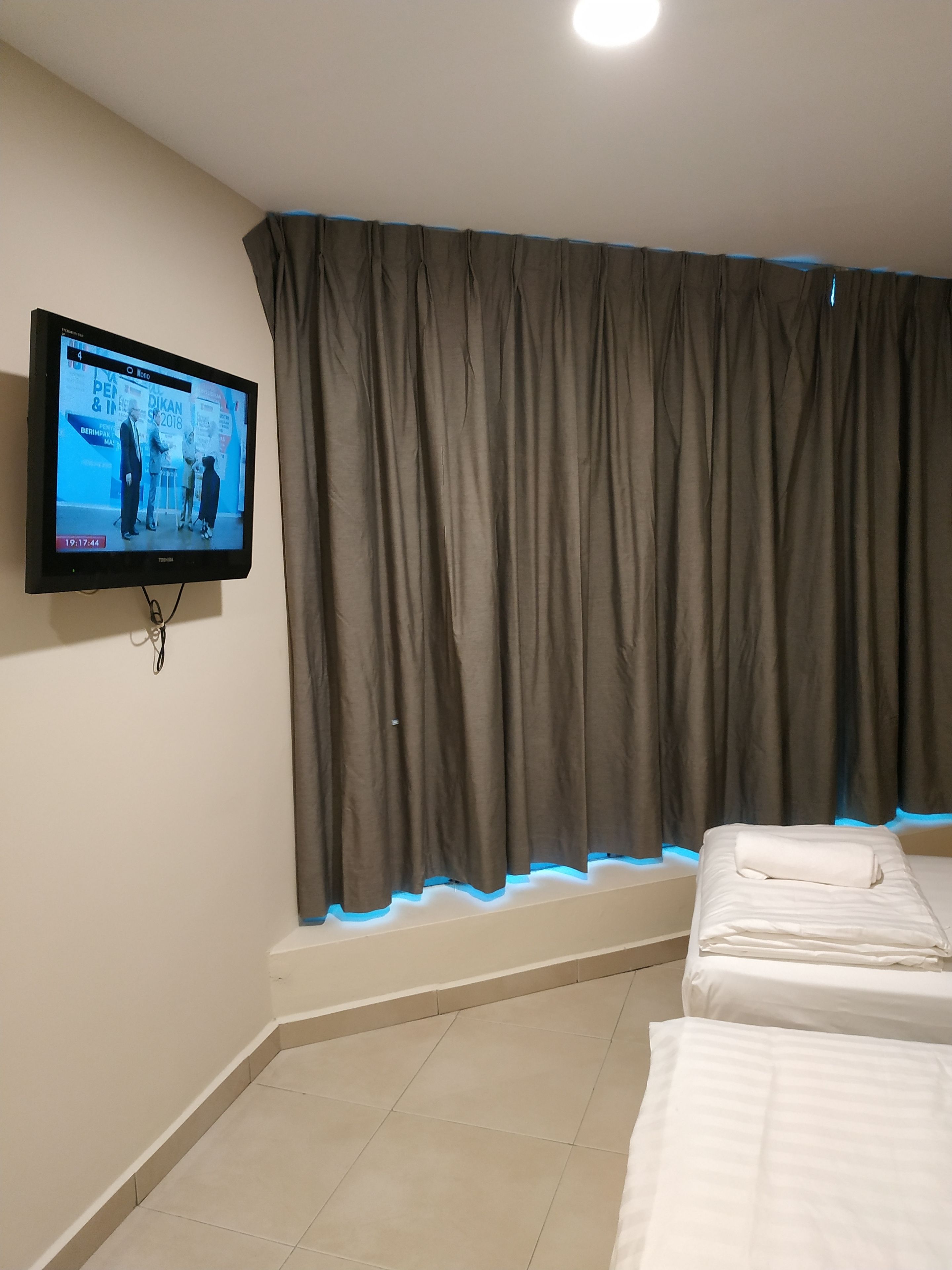 A hotel room with a television mounted on the wall, a window with curtains, and two beds with white bedding.