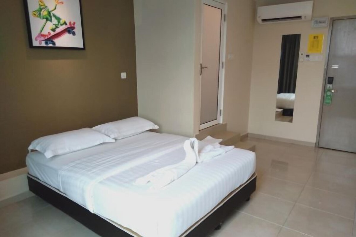 Una habitación de hotel con cama, puerta, aire acondicionado y una ventana pequeña.