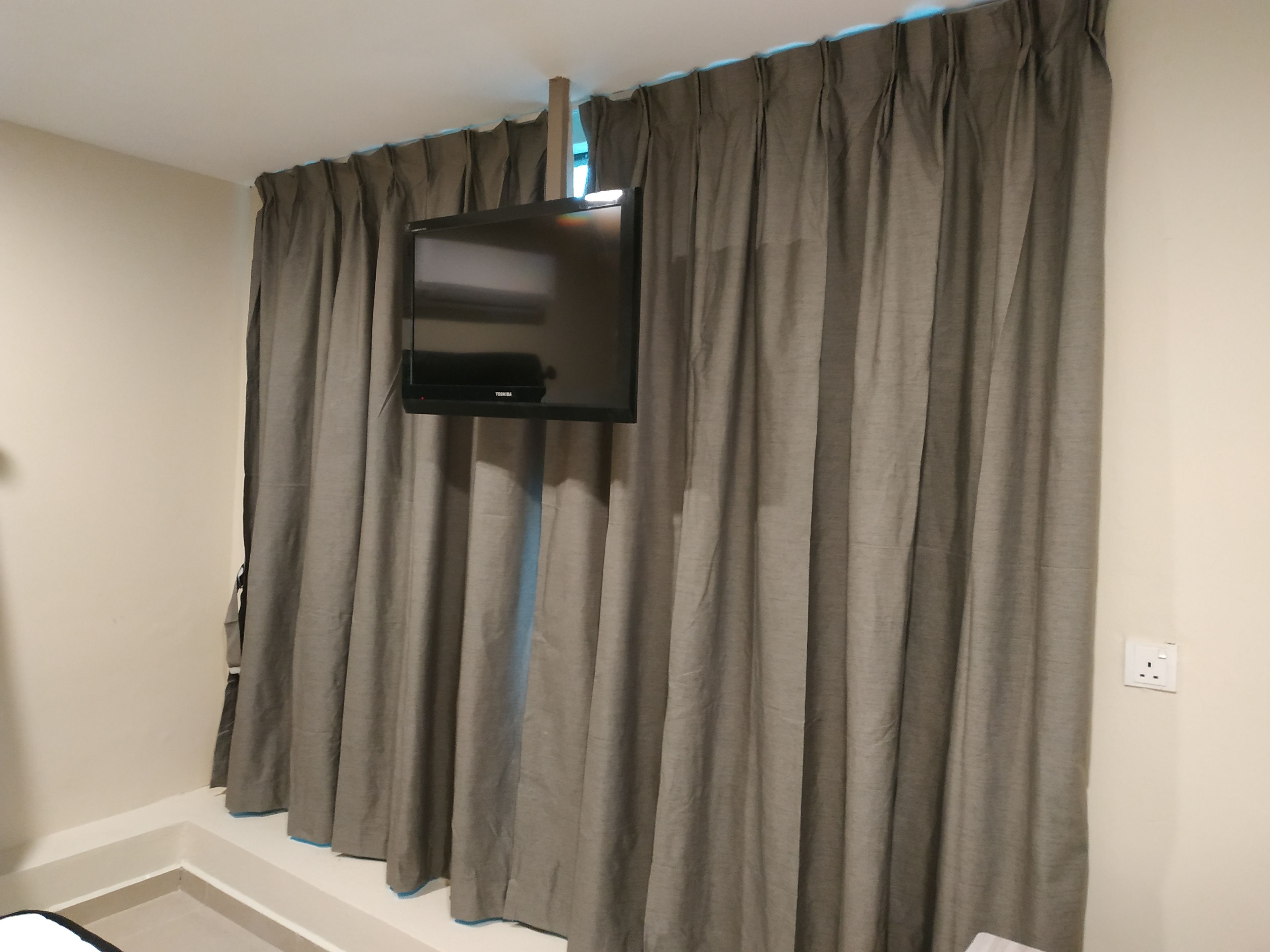 Une pièce dotée d’un téléviseur à écran plat fixé au mur, de rideaux gris et d’un plafond blanc.