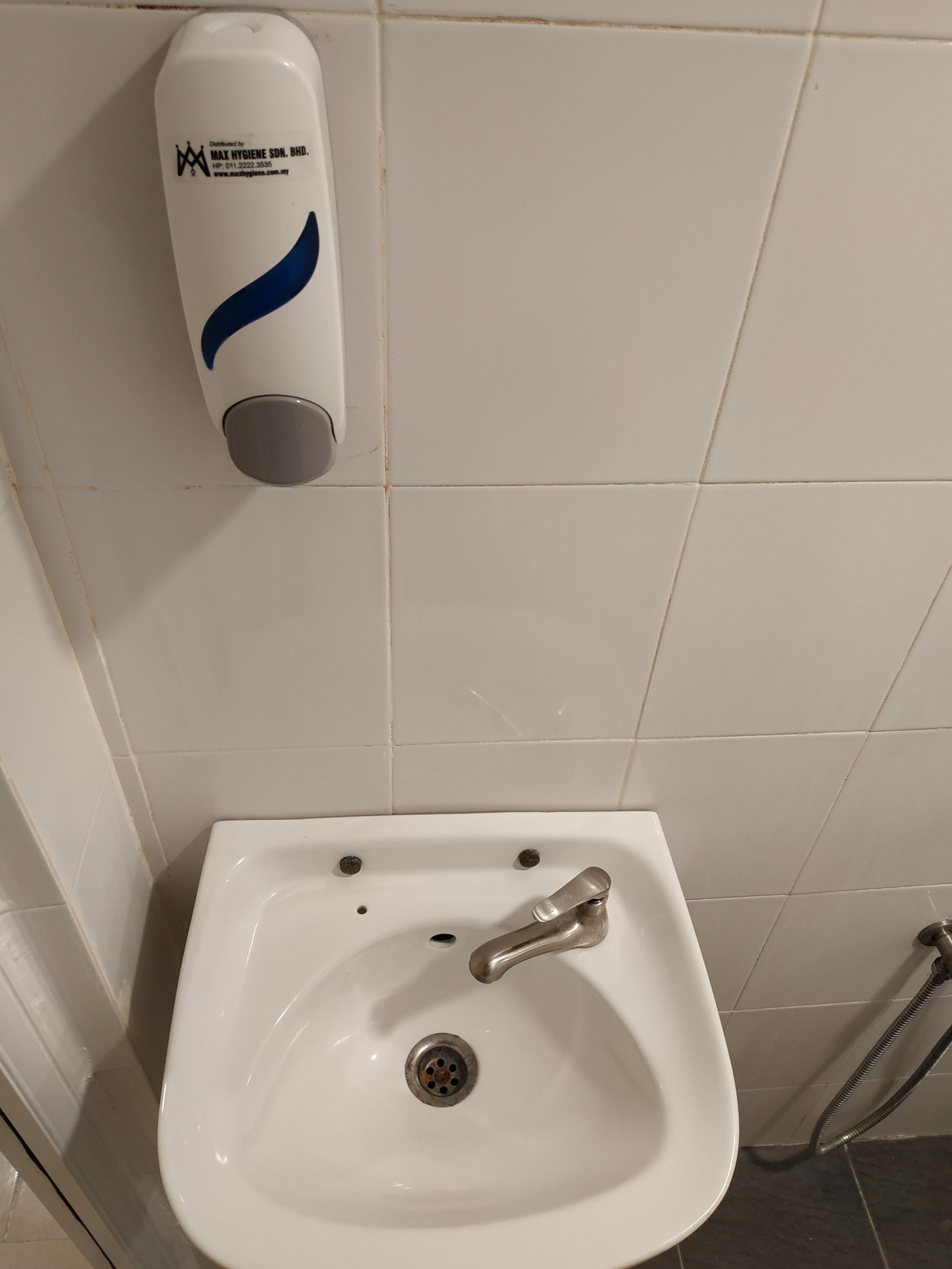 A white bathroom sink with a chrome faucet, a soap dispenser on the wall, and a shower hose.