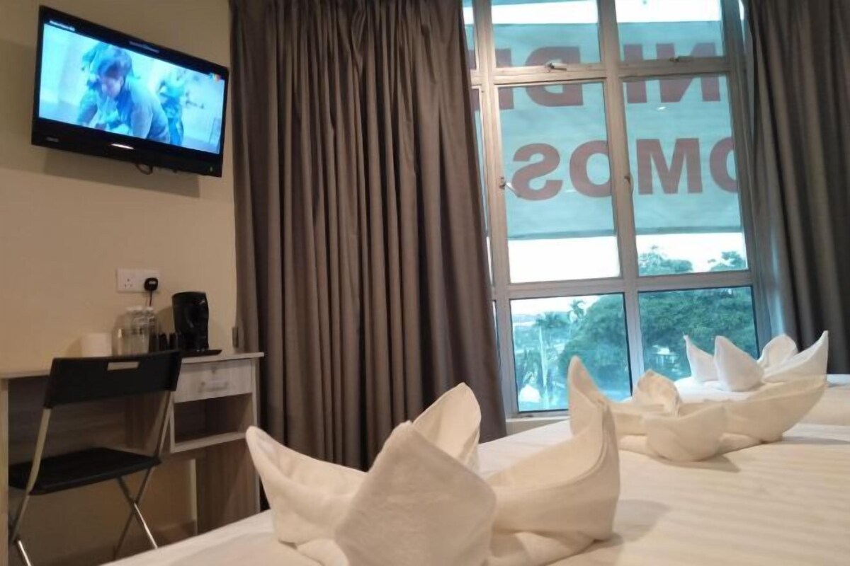 A hotel room with a bed, a desk, a chair, a television, and a window with curtains.