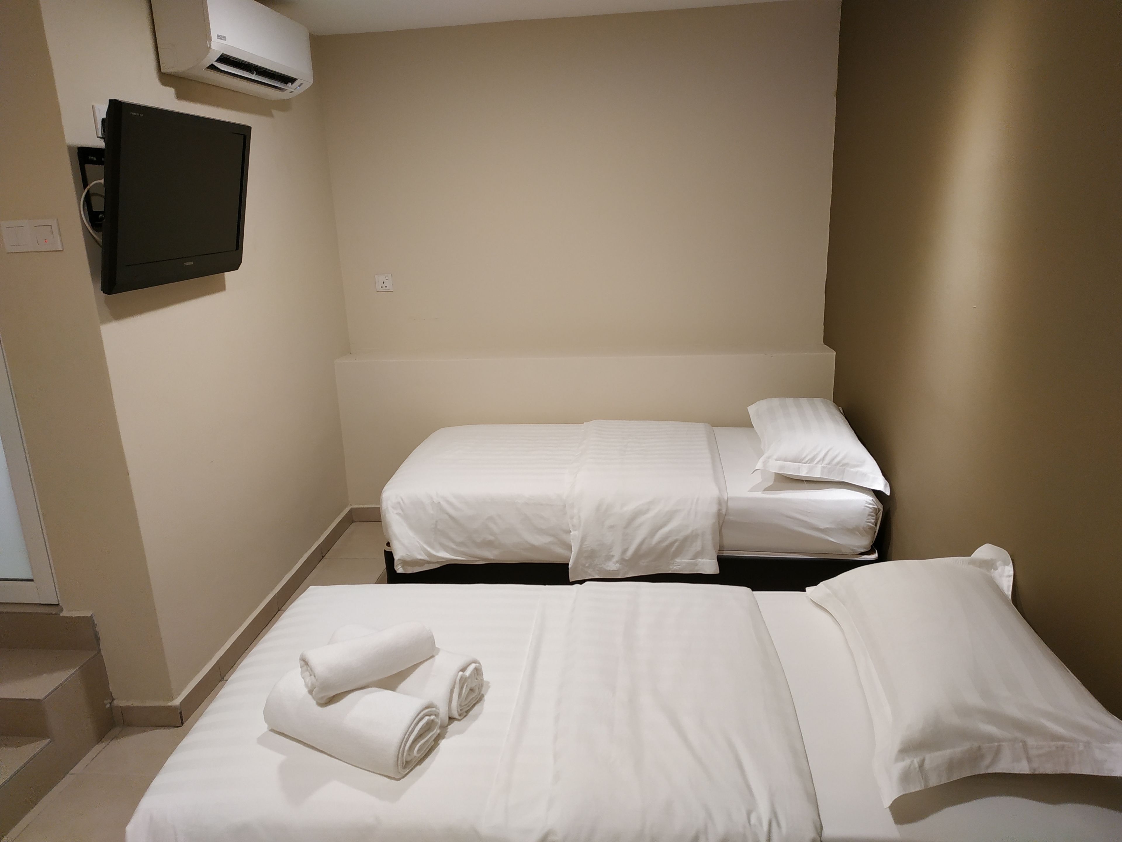 A hotel room with two beds, a flat-screen TV, and an air conditioning unit.