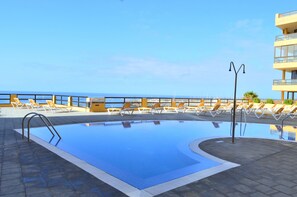 Piscina con tumbonas y vista al mar.