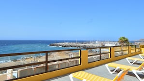 A balcony with yellow and white sun loungers overlooking a rocky coastline with a view of the sea and a distant cityscape. - APARTMENT WITH PRIVATE SOLARIUM ON THE LAST FLOOR, WiFi, HEATED POOLS, (TENERIFE)