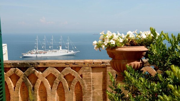 Enjoy breathtaking views of the ocean from this balcony, featuring a sailing ship in the distance and a beautiful floral display.
