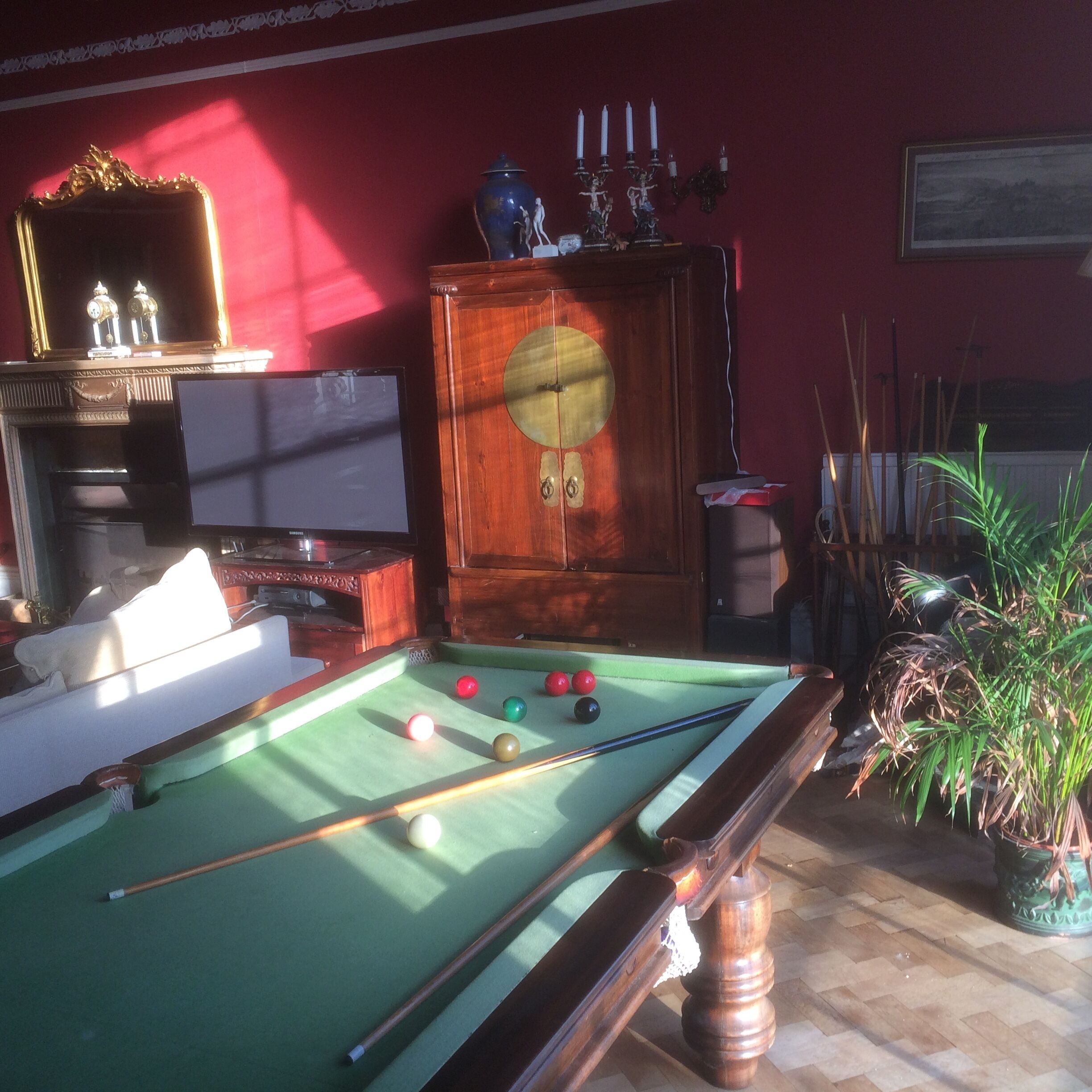 Ein Billardtisch mit Kugeln und Spielstöcken, eine Uhr und eine Vitrine mit einer Uhr.
