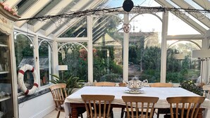 Une véranda équipée d’une table et de chaises, entourée de murs de verre qui offrent une vue sur un jardin.