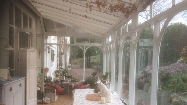 Une véranda avec une table dressée pour le repas, entourée de plantes en pot et offrant une vue sur le jardin.