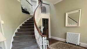 Un magnifique escalier en bois, doté d’une rampe et de balustres blanches, mène à un palier où se trouvent une porte et un miroir accroché au mur.