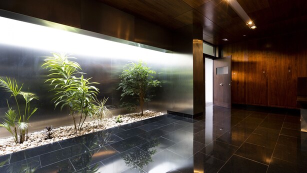 A modern lobby with a reflective black floor, a stainless steel wall, and wooden paneling.