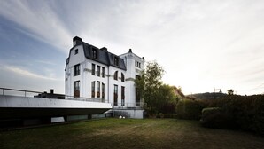 A modern two-story building with a flat roof and large windows, surrounded by a well-maintained lawn and a hedge.
