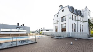 A rooftop terrace with a swimming pool, wooden deck, and a white building with large windows and balconies.