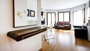 A modern living room with a large mirror, wooden console table, and a grey sofa with a red cushion.