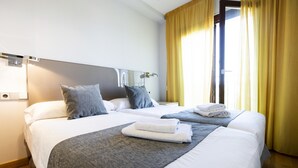 A hotel room with two beds, a large mirror, and a window with yellow curtains.