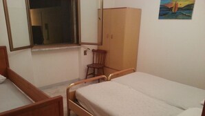 Une chambre avec un lit simple, une armoire en bois, une chaise et une fenêtre.