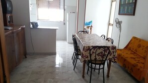 Un coin repas avec une table recouverte d’une nappe à motifs floraux, entourée de chaises. Un canapé est placé sur le côté droit.