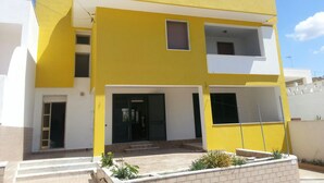 Un immeuble de deux étages avec une façade jaune, une porte noire et un petit balcon à l’étage supérieur.