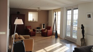 Amplia sala de estar con piso de madera, un sofá, un sillón rojo, una lámpara, una estatua y un ventanal con vistas.