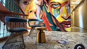 Un vestíbulo con diseño moderno, que incluye una escalera, un mural abstracto colorido, una silla azul, una mesita y un suelo estampado.