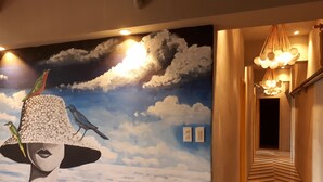 Un pasillo con un mural de una mujer con sombrero y pájaros, una escalera con piso estampado y un candelabro colgante.