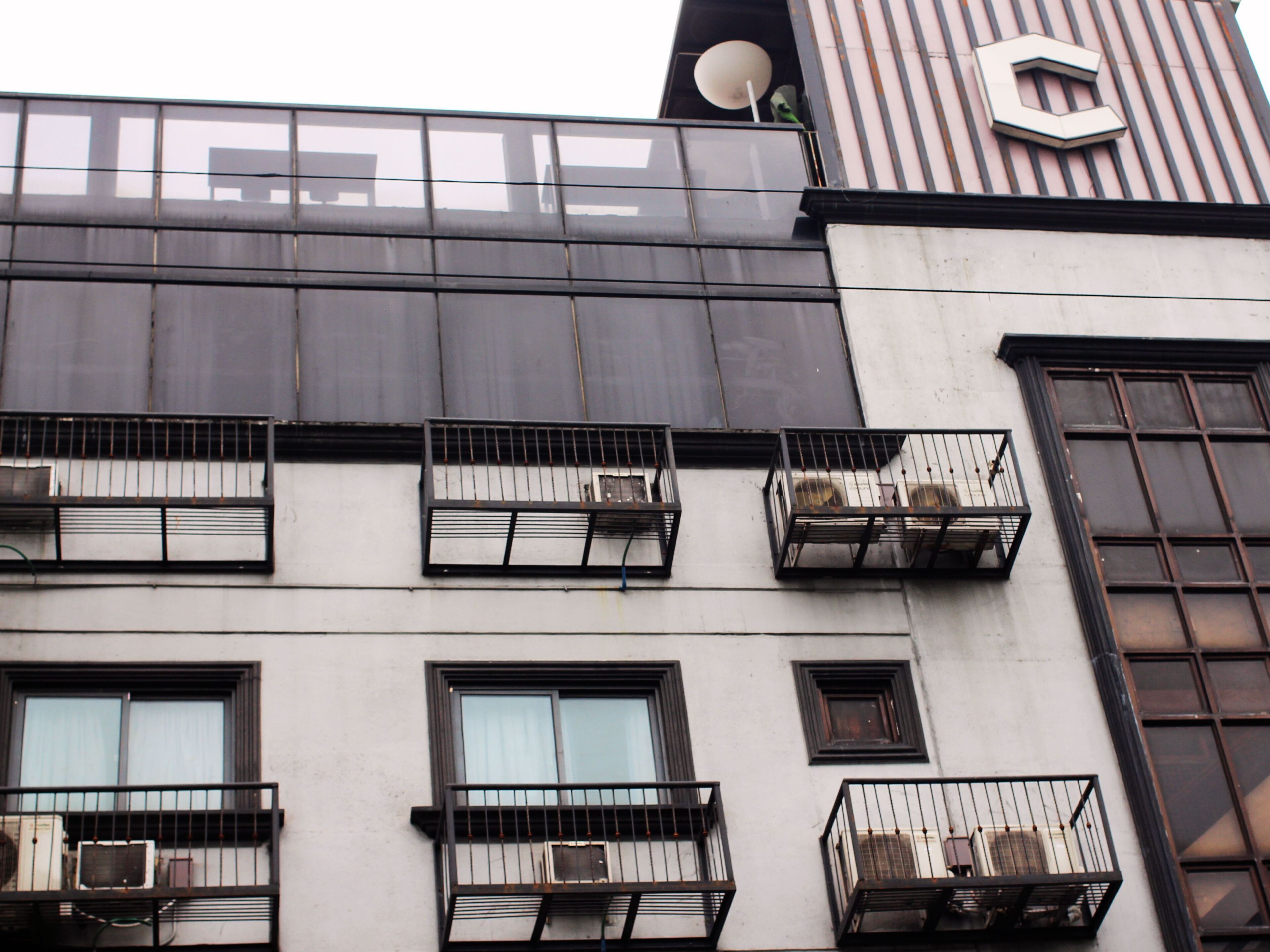 A building with multiple balconies, air conditioning units, and a large window with a curtain.