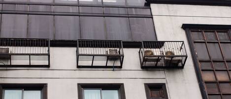 A building with multiple balconies, air conditioning units, and a large window with a curtain.