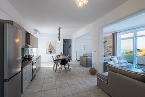 A modern kitchen with a dining area, a sofa with a view, and a stone wall.