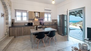 A modern kitchen with a stone wall, wooden cabinets, and a dining area with two chairs. - Paros Nereids Villas Estate with private pools and amazing  view (Paros)