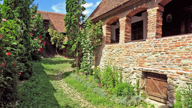 Ein rustikales Steinhaus mit Backsteinschornstein, umgeben von einem Garten mit verschiedenen Pflanzen und Blumen.