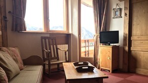 A cozy room with a wooden sofa, a wooden table, a chair, a television on a wooden cabinet, and a window with curtains.