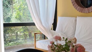 A room with a wooden table, a white bed with white pillows, a round mirror on the wall, and a window with white curtains. - Vacation House "La Caprignola" (Buccino)