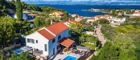 A modern villa with a swimming pool, surrounded by lush greenery and a view of the sea.